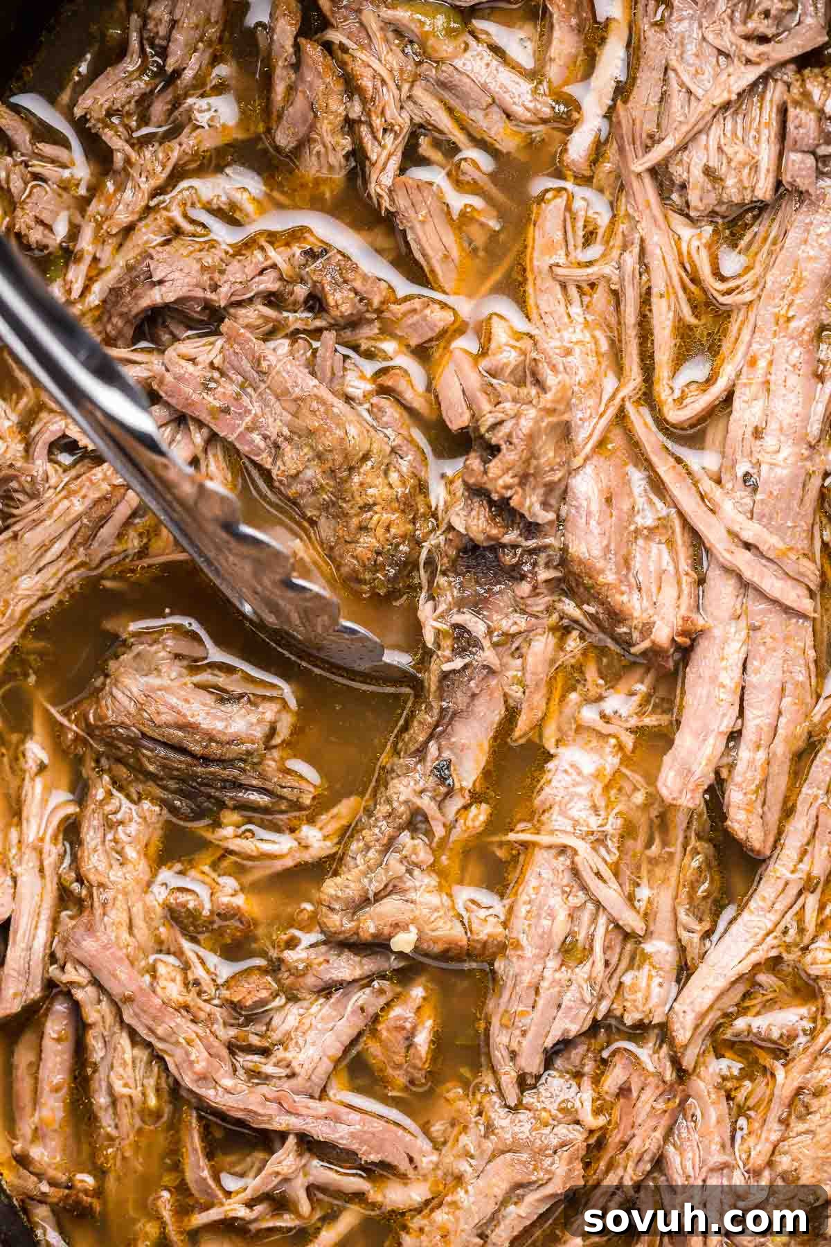 Tender Crock Pot Italian Beef in a slow cooker with tongs, ready to be shredded.