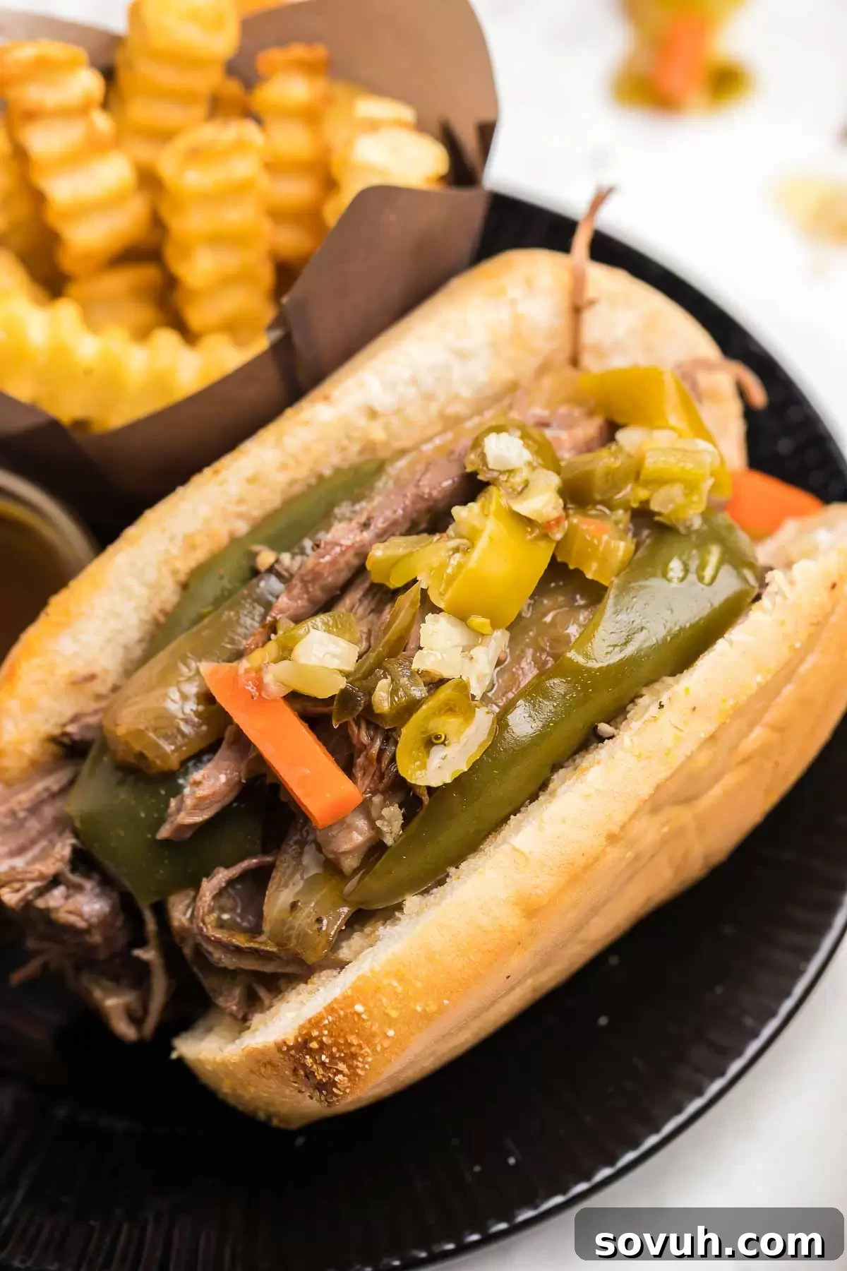 A close-up of a Crock Pot Italian Beef sandwich with peppers, showing the juicy shredded beef.