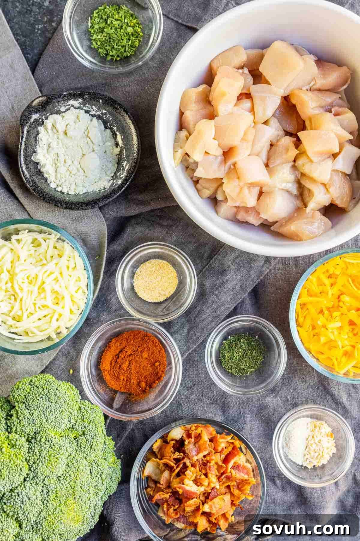 A selection of fresh ingredients including chicken breast, broccoli florets, crispy bacon, blocks of cheddar, mozzarella, and cream cheese, olive oil, and ranch seasoning, ready for making Keto Chicken Bacon Ranch Casserole