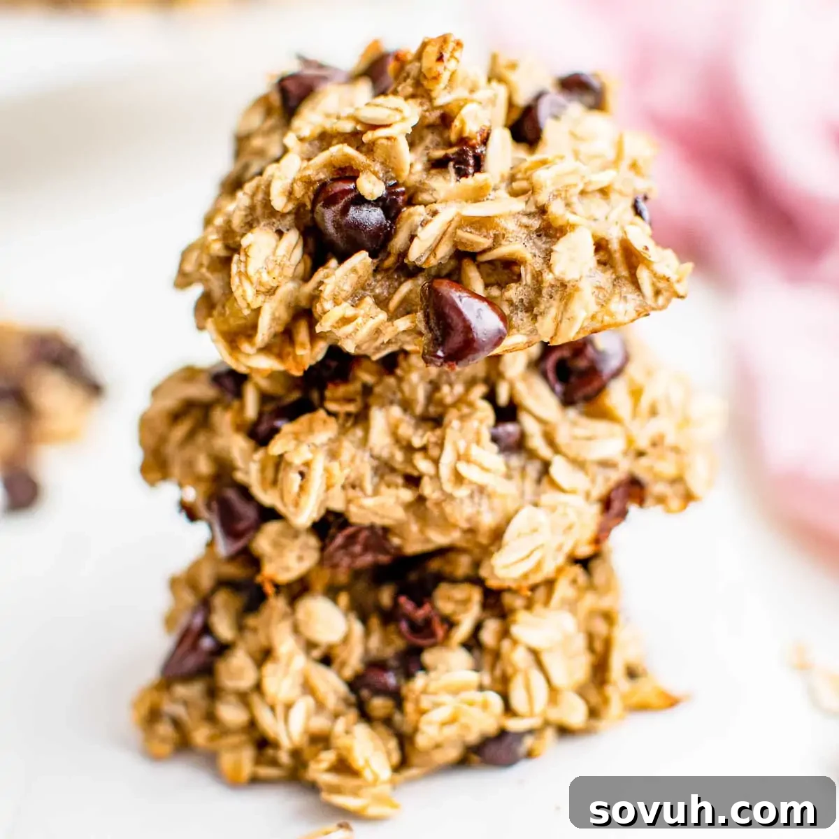 A stack of three oatmeal cookies with chocolate chips on a light background, highlighting their healthy appeal.