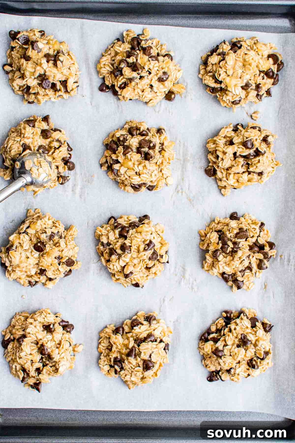 Twelve unbaked oatmeal chocolate chip cookies on a parchment-lined baking sheet, ready for baking.