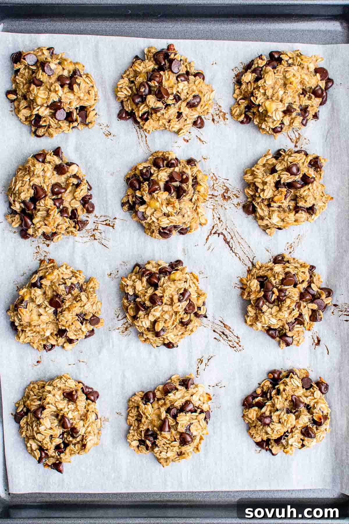 A baking sheet with twelve chocolate chip oatmeal cookies on parchment paper, ready to be baked, showcasing the perfectly portioned dough.