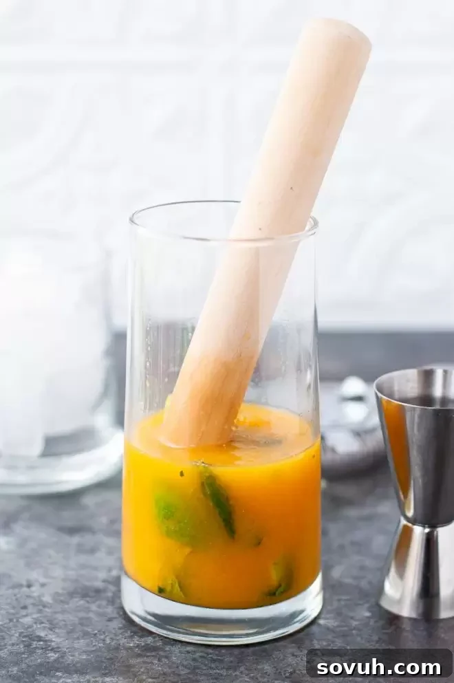 Hands actively muddling fresh mint and lime with passion fruit puree in a cocktail shaker for a vibrant mojito.