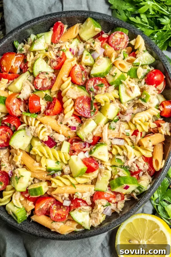 A large bowl of colorful no-mayo tuna pasta salad garnished with fresh lemon and parsley