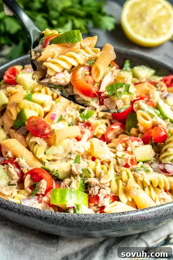 Tossing a large bowl of fresh tuna pasta salad with a serving spoon