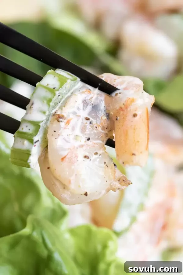 A fork lifts a generous bite of creamy shrimp salad, showcasing its textures and vibrant color.