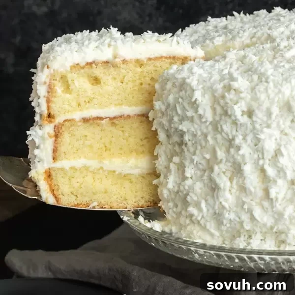 Slice of coconut cake being cut from a three-layer coconut cake, showing moist layers and fluffy frosting.