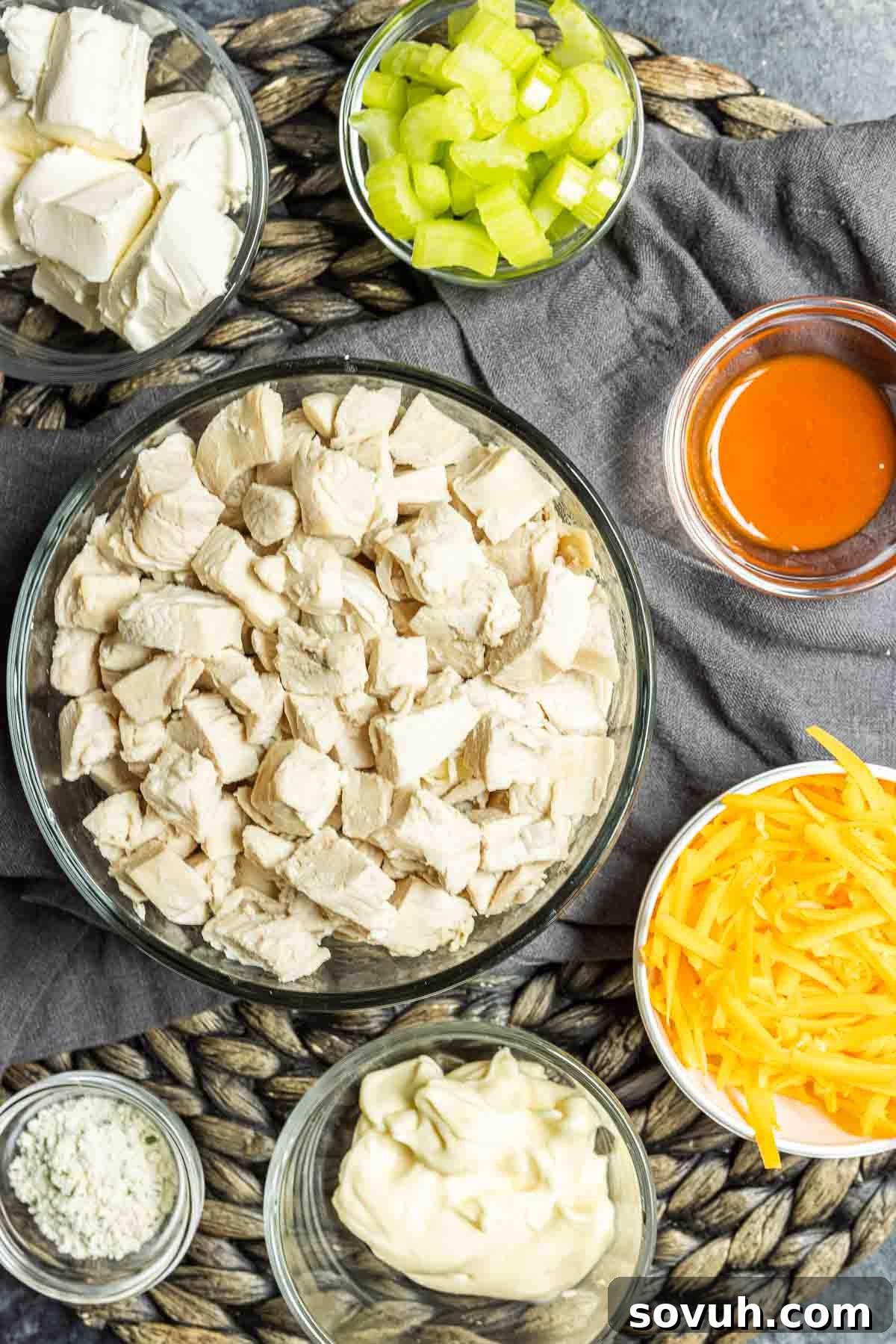 Ingredients for Buffalo Chicken Salad laid out on a table: cooked chicken, mayonnaise, buffalo sauce, ranch seasoning, celery, and shredded cheddar cheese.