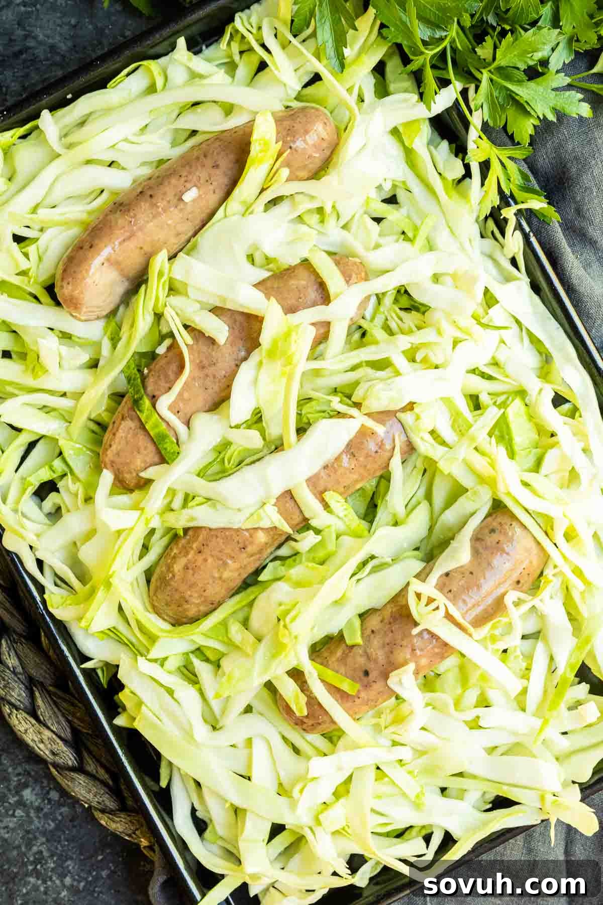 A sheet pan with uncooked, thinly sliced cabbage and sausage links, ready for the oven.