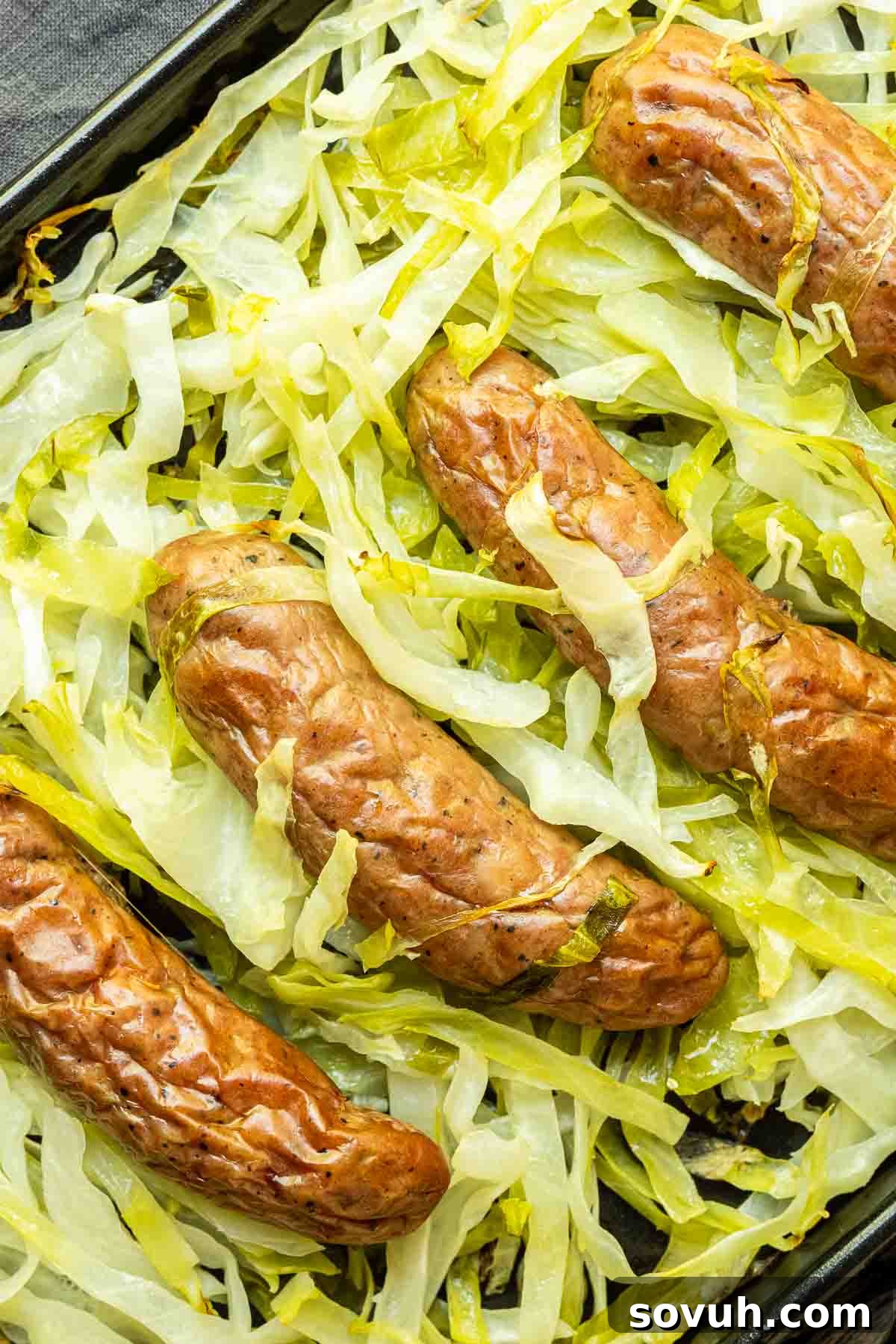 Cooked Sheet Pan Sausage and Cabbage displayed beautifully on a black sheet pan, ready to serve.