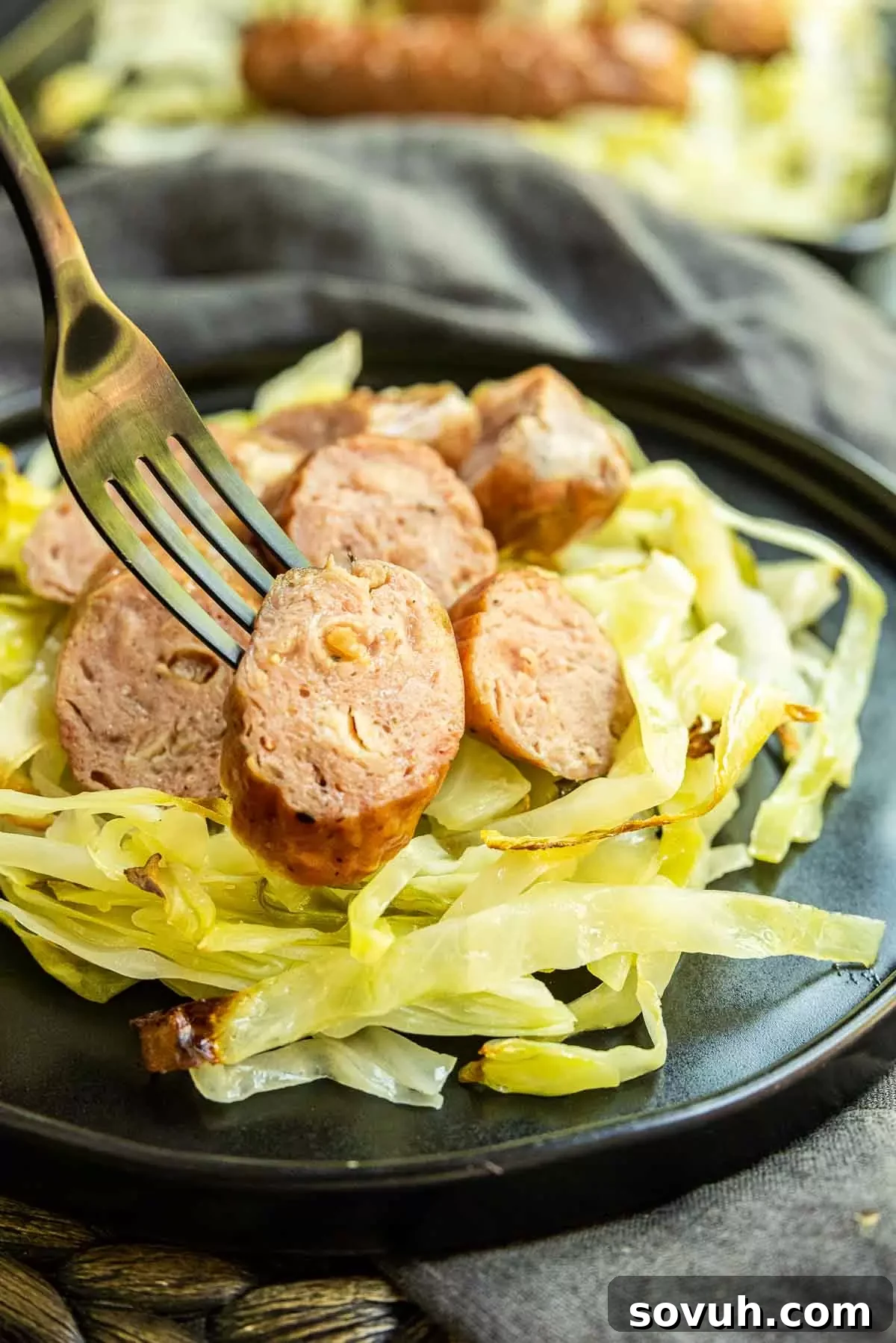 A fork holding a piece of sausage and a generous amount of tender cabbage, showcasing the appetizing texture of the dish.