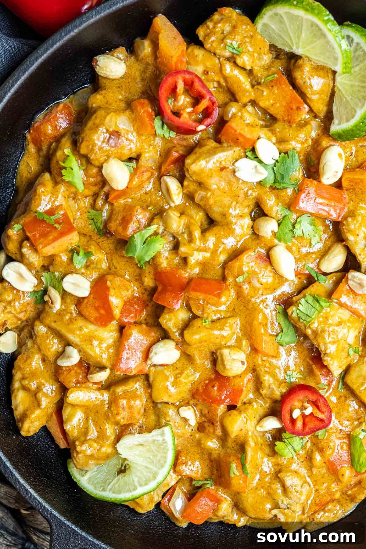 Keto Peanut Butter Chicken in a skillet garnished with chopped peanuts and fresh lime wedges.