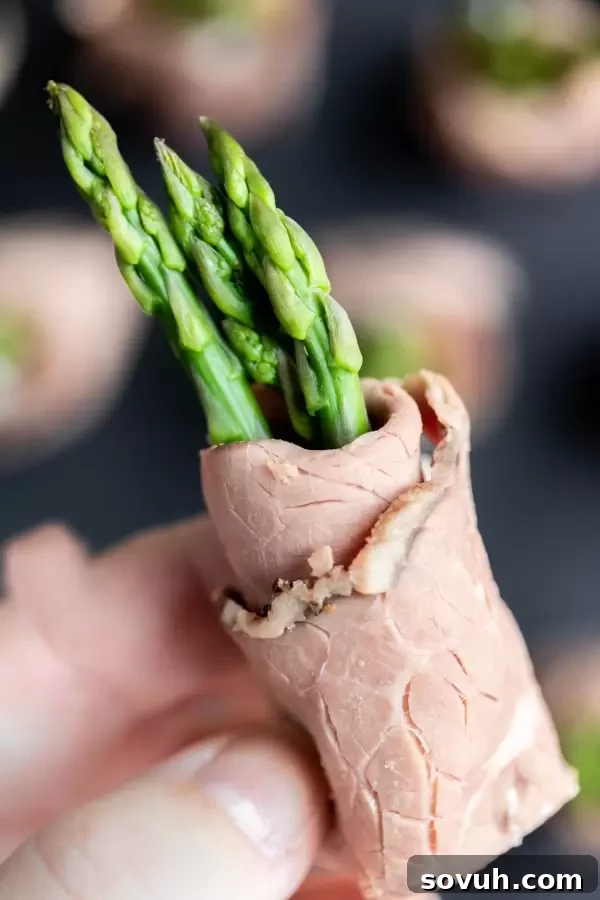 A hand holding appetizer sized Roast Beef and Asparagus Roll Ups