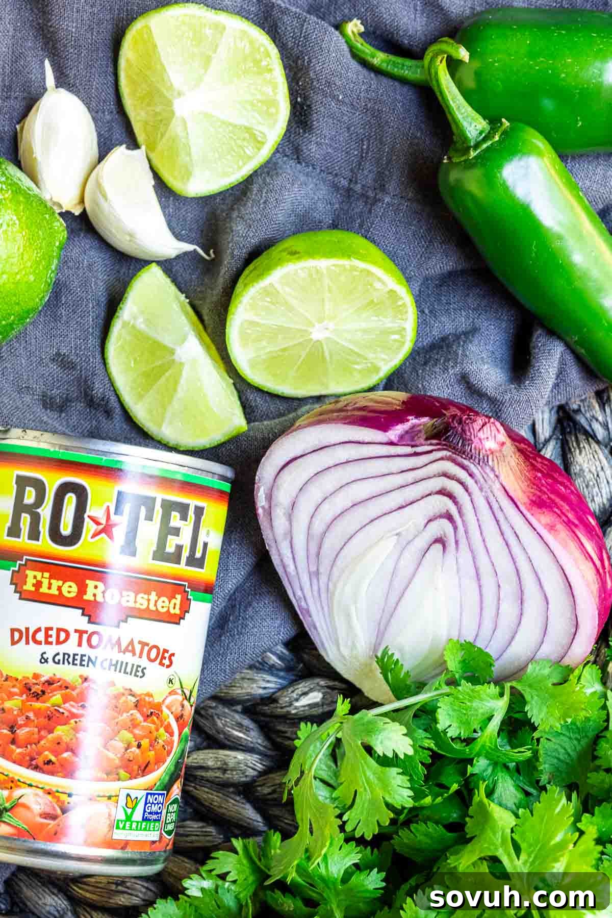 All the fresh ingredients for making Rotel salsa laid out on a cutting board, including Rotel cans, red onion, garlic, jalapeño, cilantro, and lime.