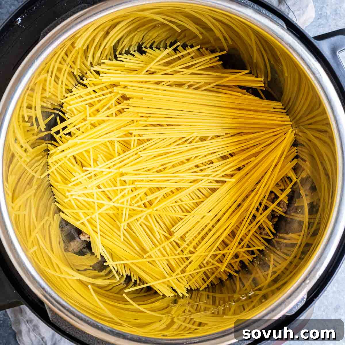Effortless Instant Pot Spaghetti 5 Adding broken spaghetti noodles to cooked meat in an Instant Pot