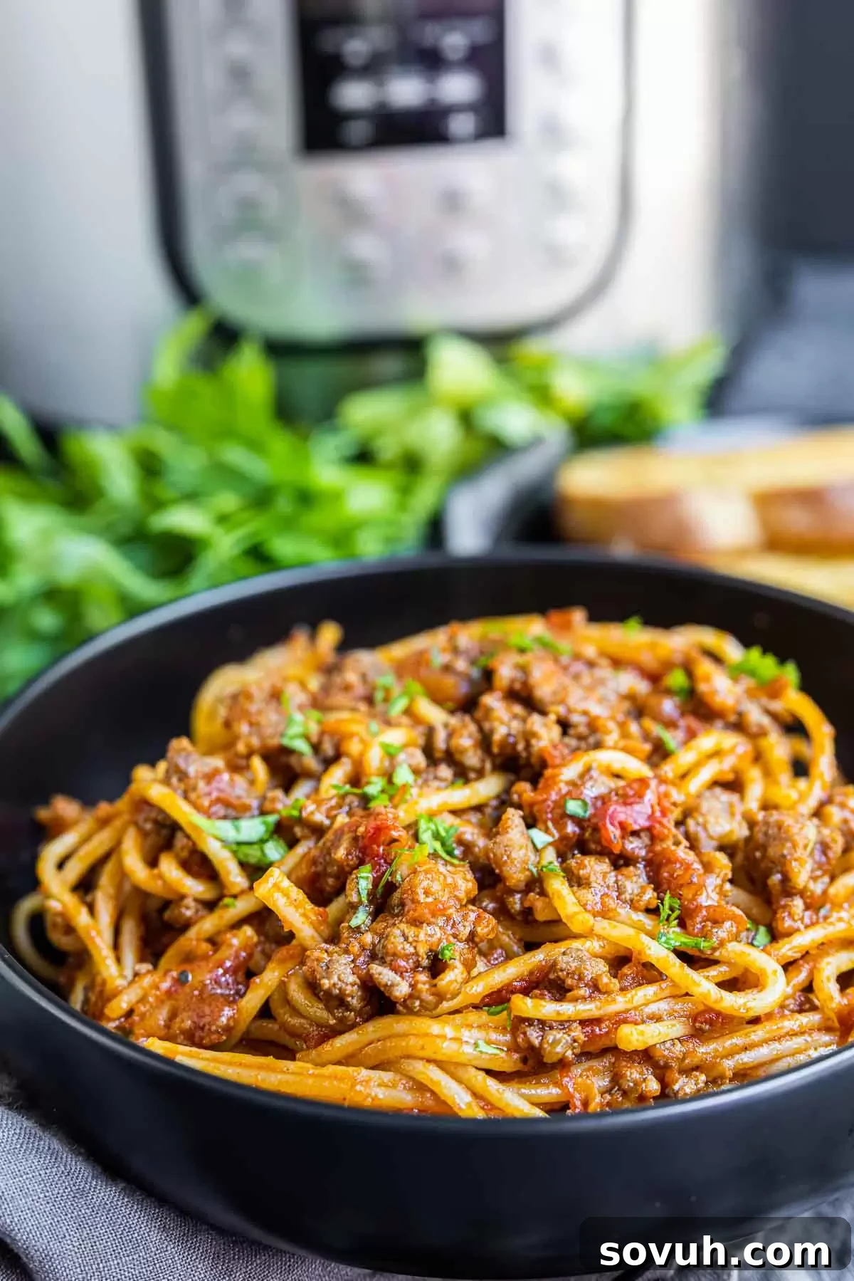 Effortless Instant Pot Spaghetti 8 Instant Pot Spaghetti in a black bowl with the Instant Pot in the background