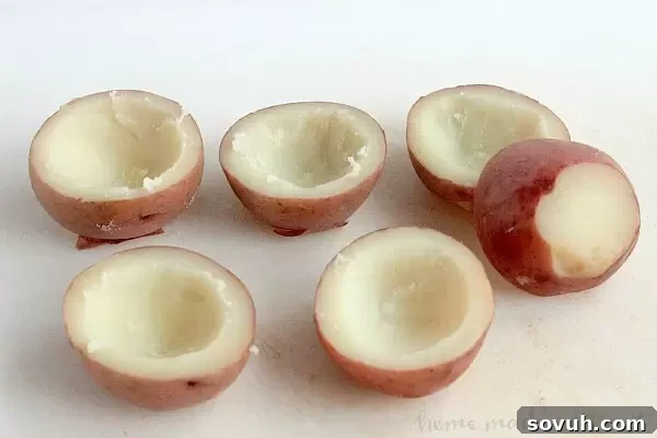 Close-up of three Irish Potato bites in different stages of preparation on a baking sheet, showing the scooped-out potato halves and the delicious filling.