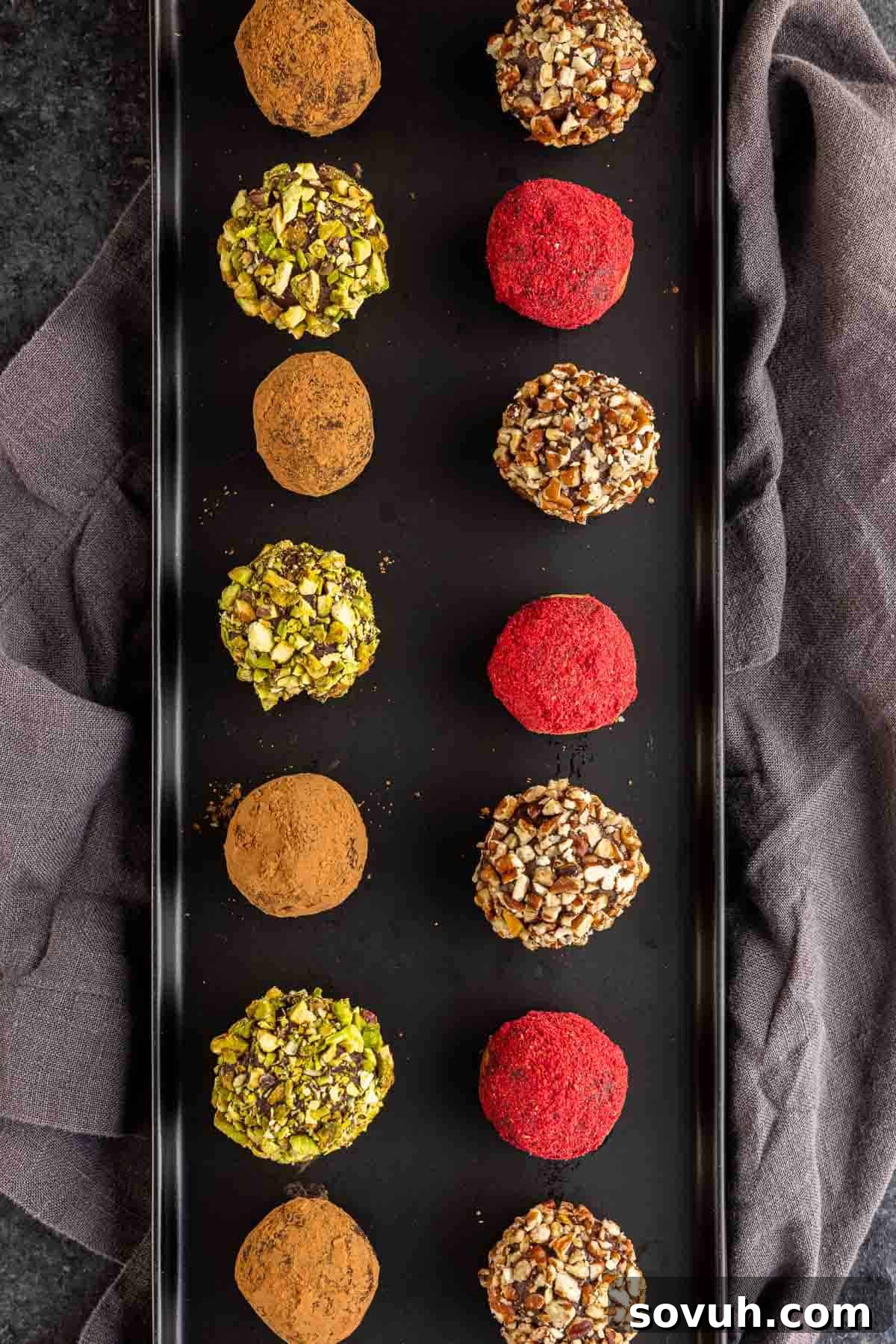 Assortment of homemade chocolate truffles beautifully arranged on a black platter, showcasing various toppings.