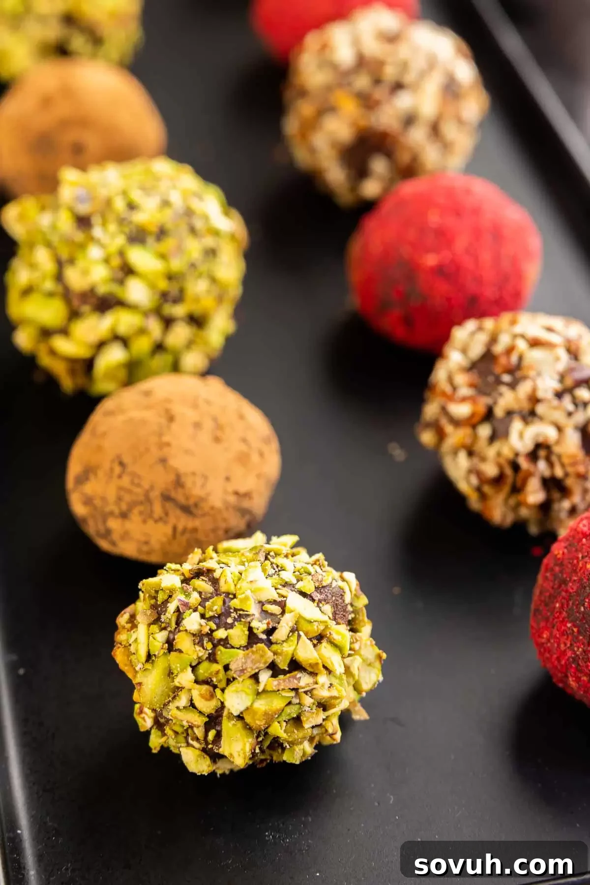 Assortment of chocolate truffles, some rolled in chopped pistachio, others in cocoa powder, beautifully presented on a dark background.