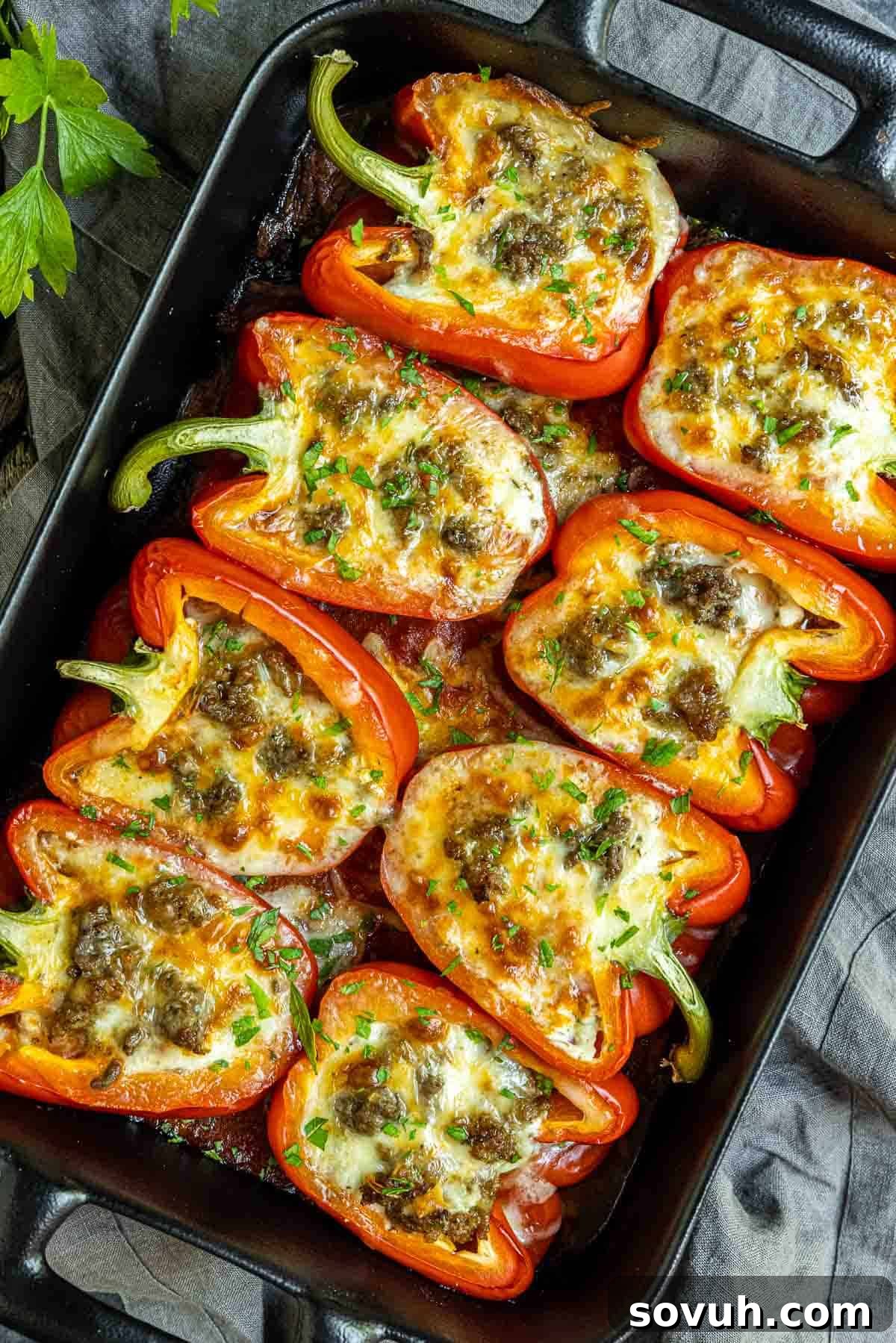 Close-up of baked Lasagna Stuffed Peppers in a black casserole dish, garnished with fresh chopped parsley.
