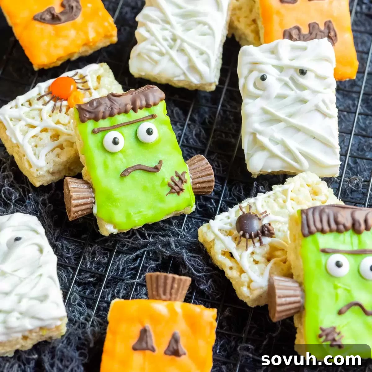 Decorated Halloween Rice Krispies Treats on a black cloth, showcasing Frankenstein, Mummy, Pumpkin, and Spider designs.