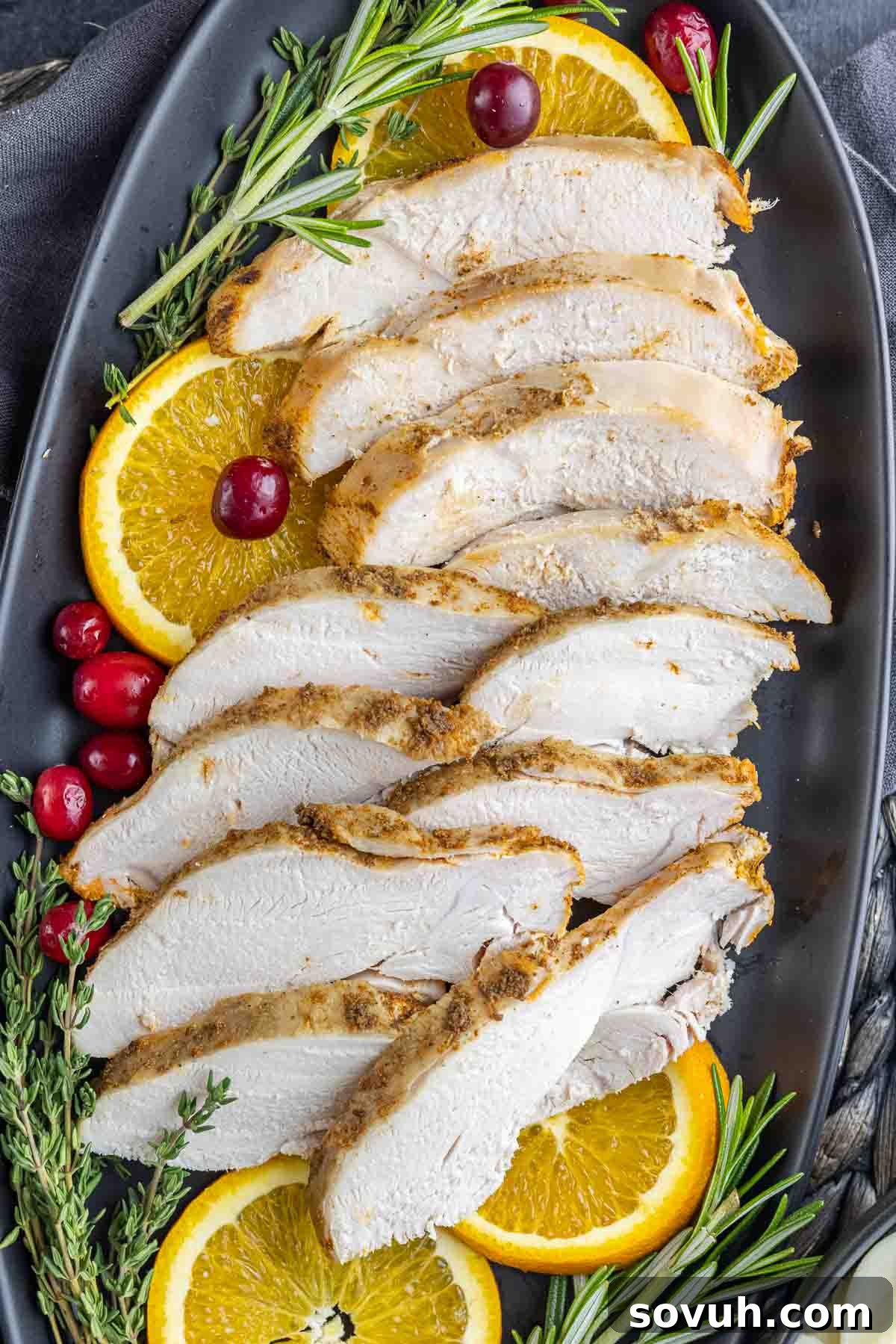 sliced Slow Cooker Turkey Breast with black platter with oranges, cranberries and rosemary