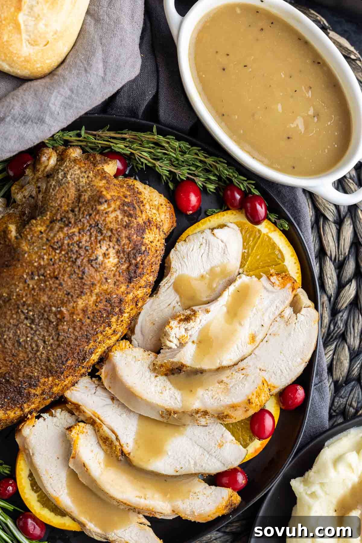 Platter with sliced roasted turkey, beautifully garnished, beside a white gravy boat filled with Homemade Turkey Gravy.