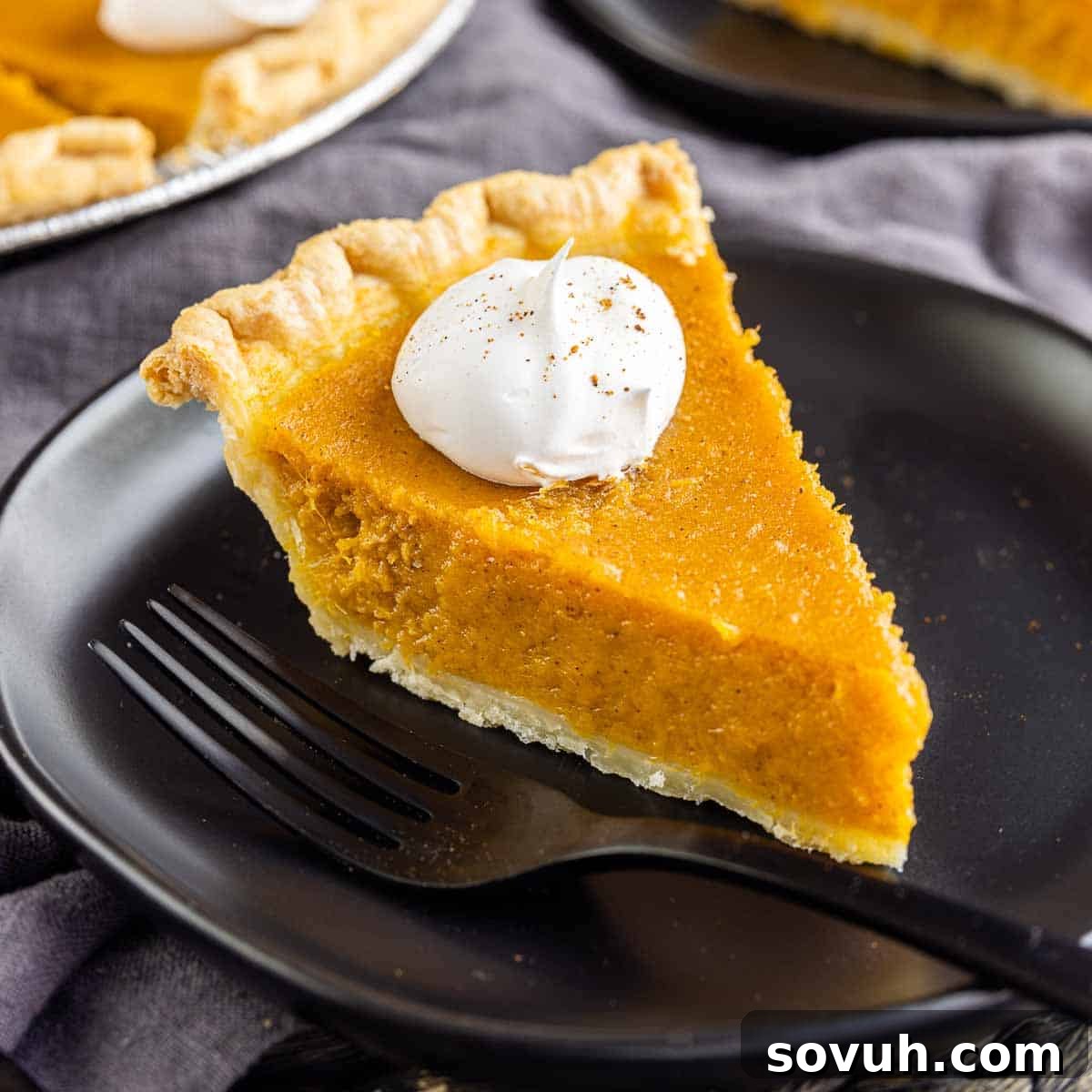 A perfectly baked sweet potato pie resting on a black plate with a fork, ready to be enjoyed.