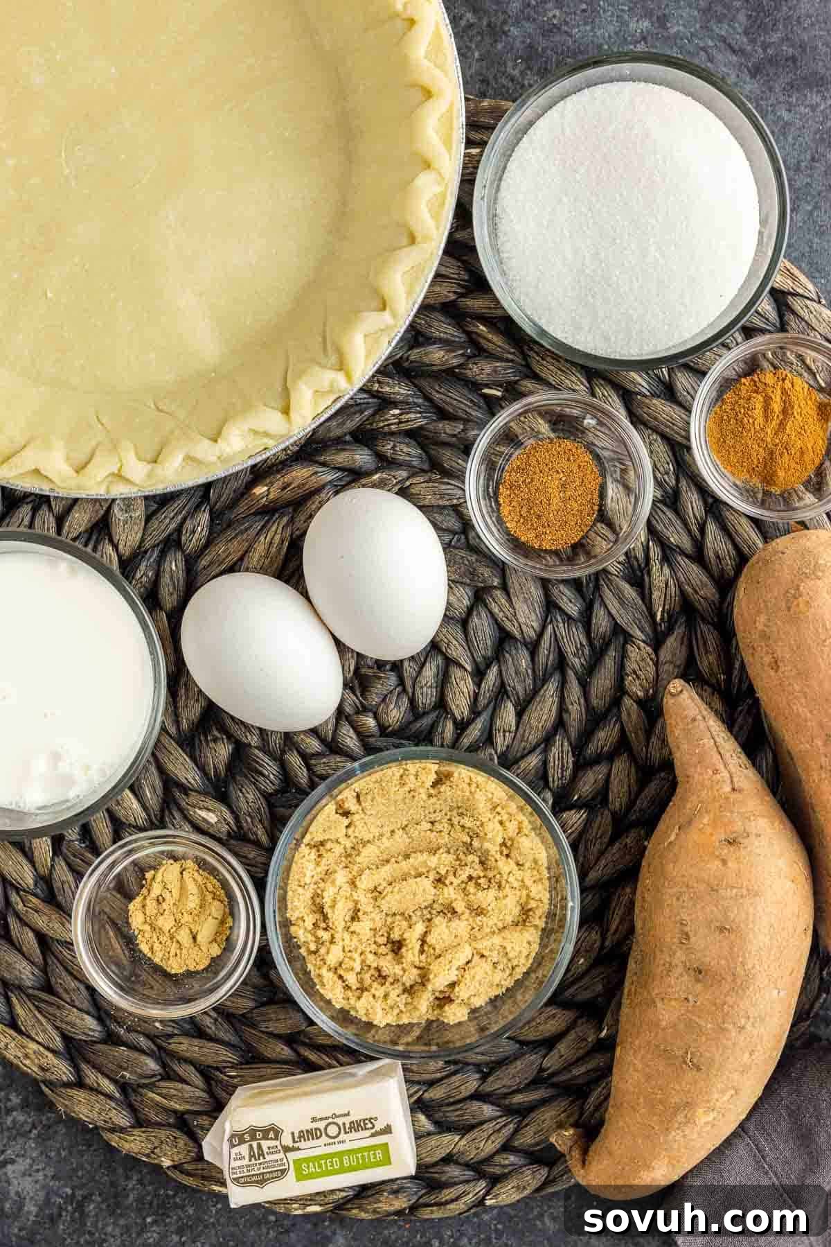 A collection of fresh sweet potatoes, eggs, butter, milk, and spices laid out as ingredients for sweet potato pie.