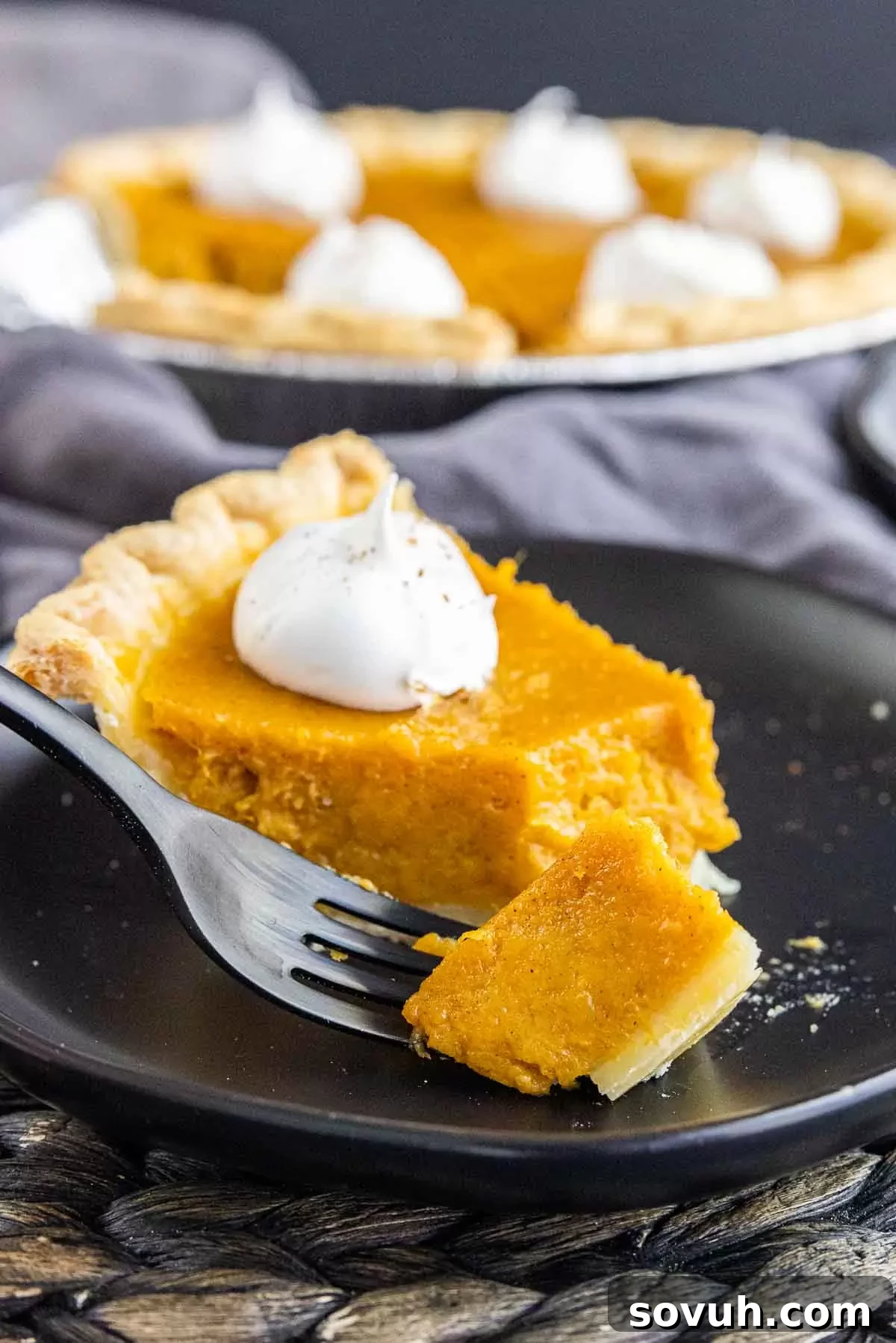 A single slice of sweet potato pie on a black plate with a matching black fork, showcasing its creamy texture.