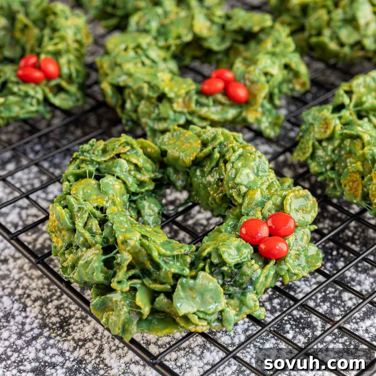 Vibrantly green Christmas Wreath Cookies made with crispy cornflakes and festive red candies, displayed artfully for the holidays.