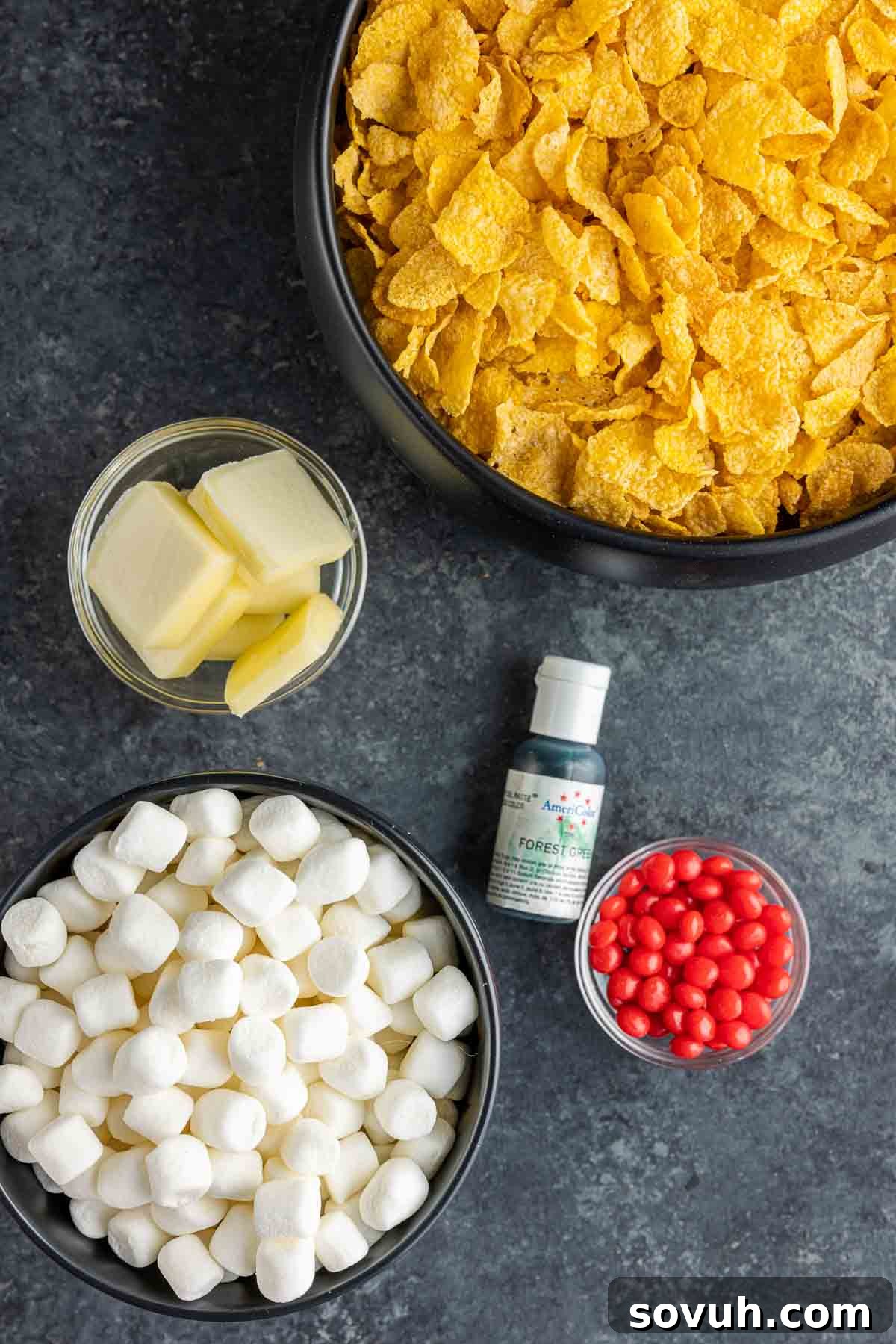 Ingredients for Easy No-Bake Christmas Wreath Cookies including butter, marshmallows, green food coloring, cornflakes, and red hot candies.