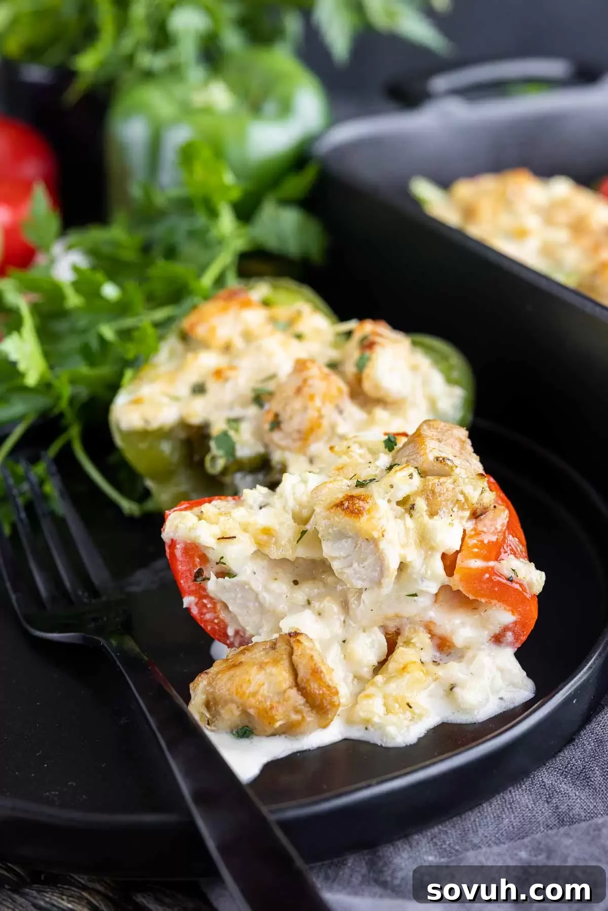 Creamy Keto Chicken Alfredo Stuffed Peppers 6 A Keto Chicken Alfredo Stuffed Pepper cut in half on a black plate, revealing the creamy filling and a fork ready to enjoy