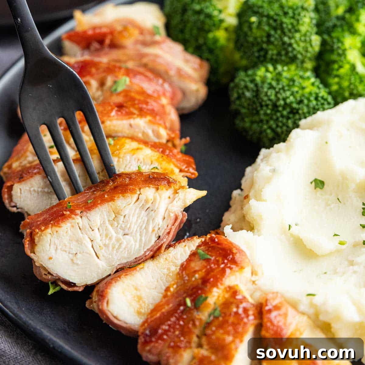 A delicious piece of Prosciutto Wrapped Chicken on a black fork, showcasing its crispy exterior and succulent interior.