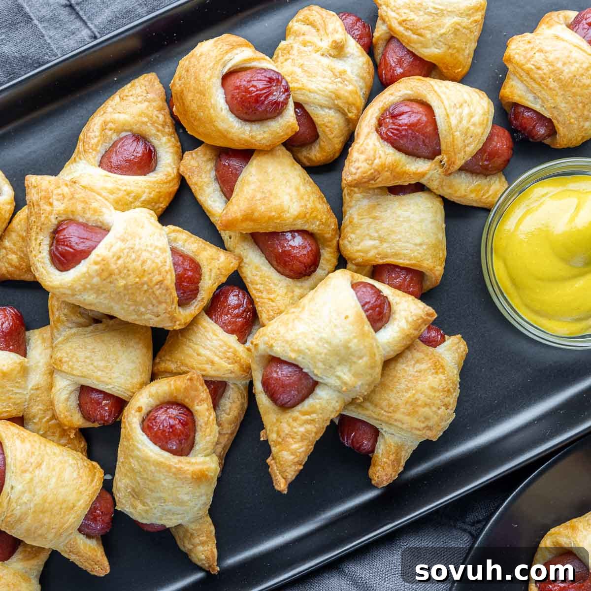 black platter of Air Fryer Pigs in a Blanket with yellow mustard on the side