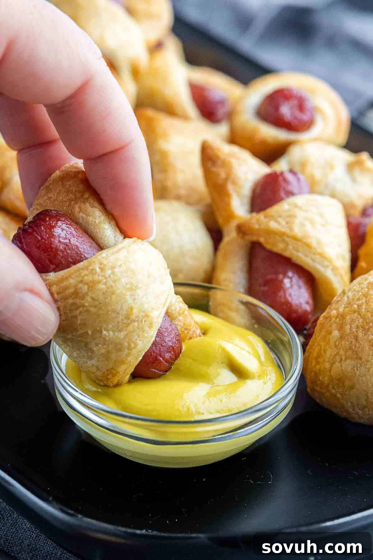 dipping Air Fryer Pigs in a Blanket in mustard