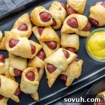 black platter of Air Fryer Pigs in a Blanket with yellow mustard on the side