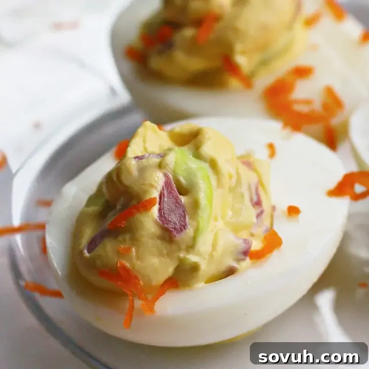 A close-up of a perfectly halved Irish deviled egg, topped with a creamy, vibrant green filling, hints of chopped red onion, and a delicate shredded carrot garnish – a festive St. Patrick’s Day appetizer.