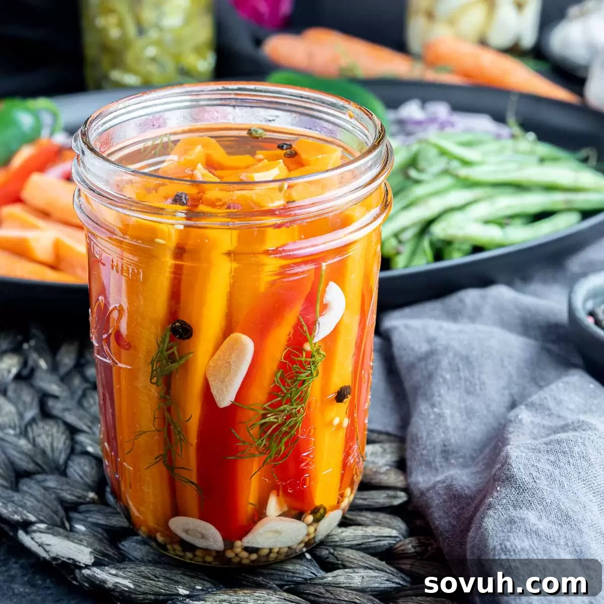 A glass jar filled with bright orange quick pickled carrots, garnished with fresh dill.