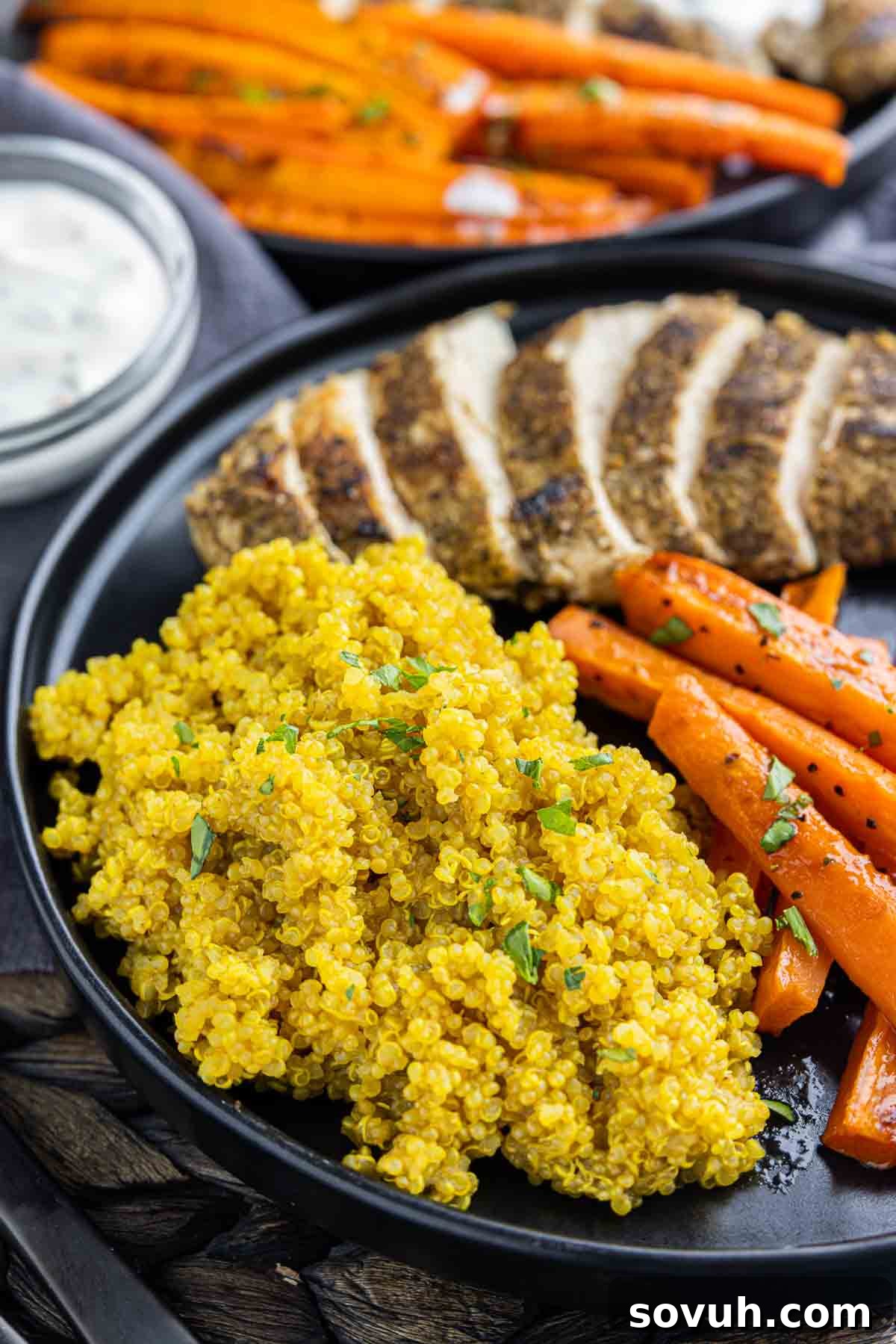 Turmeric Quinoa on a black plate with carrots and sliced chickem