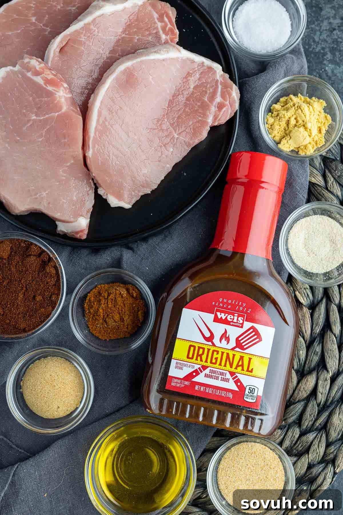 A vibrant display of fresh ingredients laid out, including boneless pork chops, olive oil, a variety of spices like chili powder and paprika, and a bottle of barbecue sauce, ready for making Air Fryer BBQ Pork Chops.