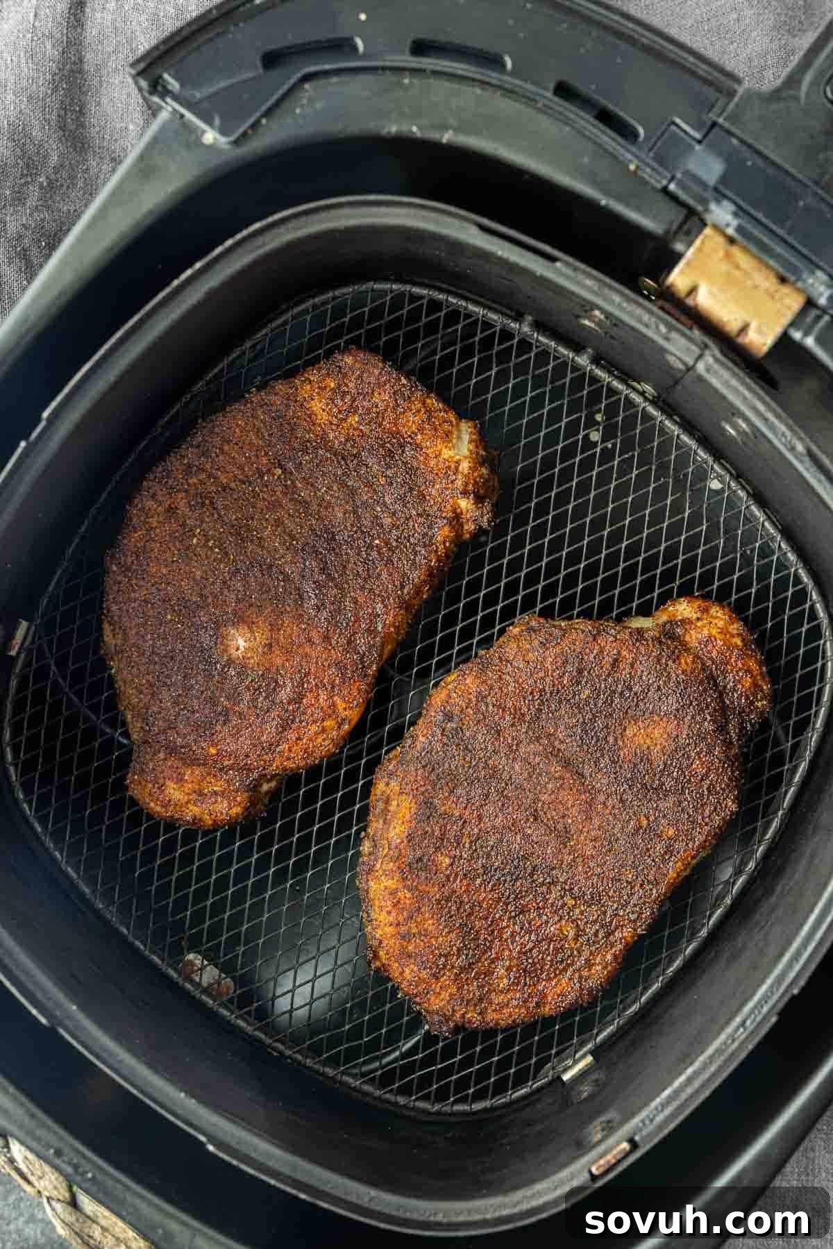 Golden-brown Air Fryer BBQ Pork Chops resting inside an air fryer basket, showing their perfectly cooked, crispy exterior.