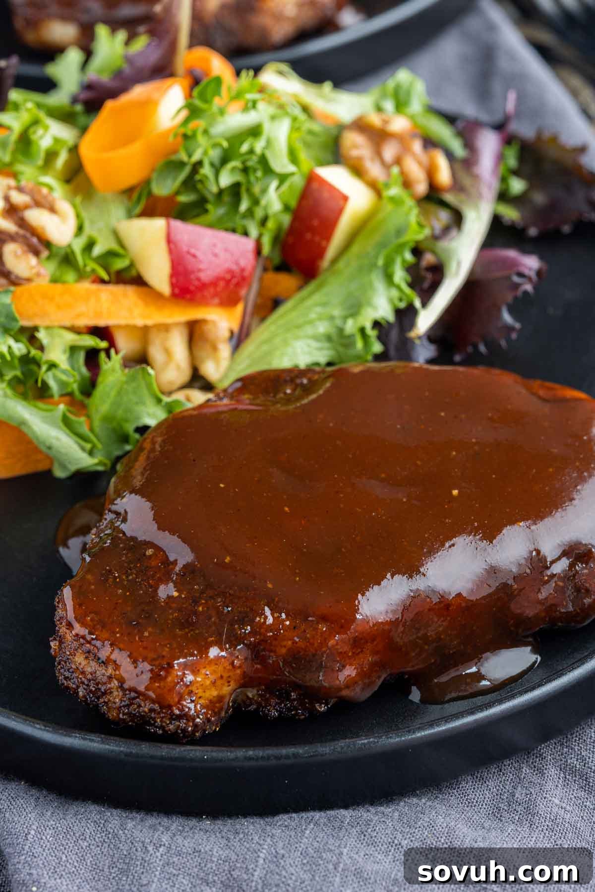 Two Air Fryer BBQ Pork Chops beautifully plated with a generous coating of rich barbecue sauce on top, ready to be enjoyed.
