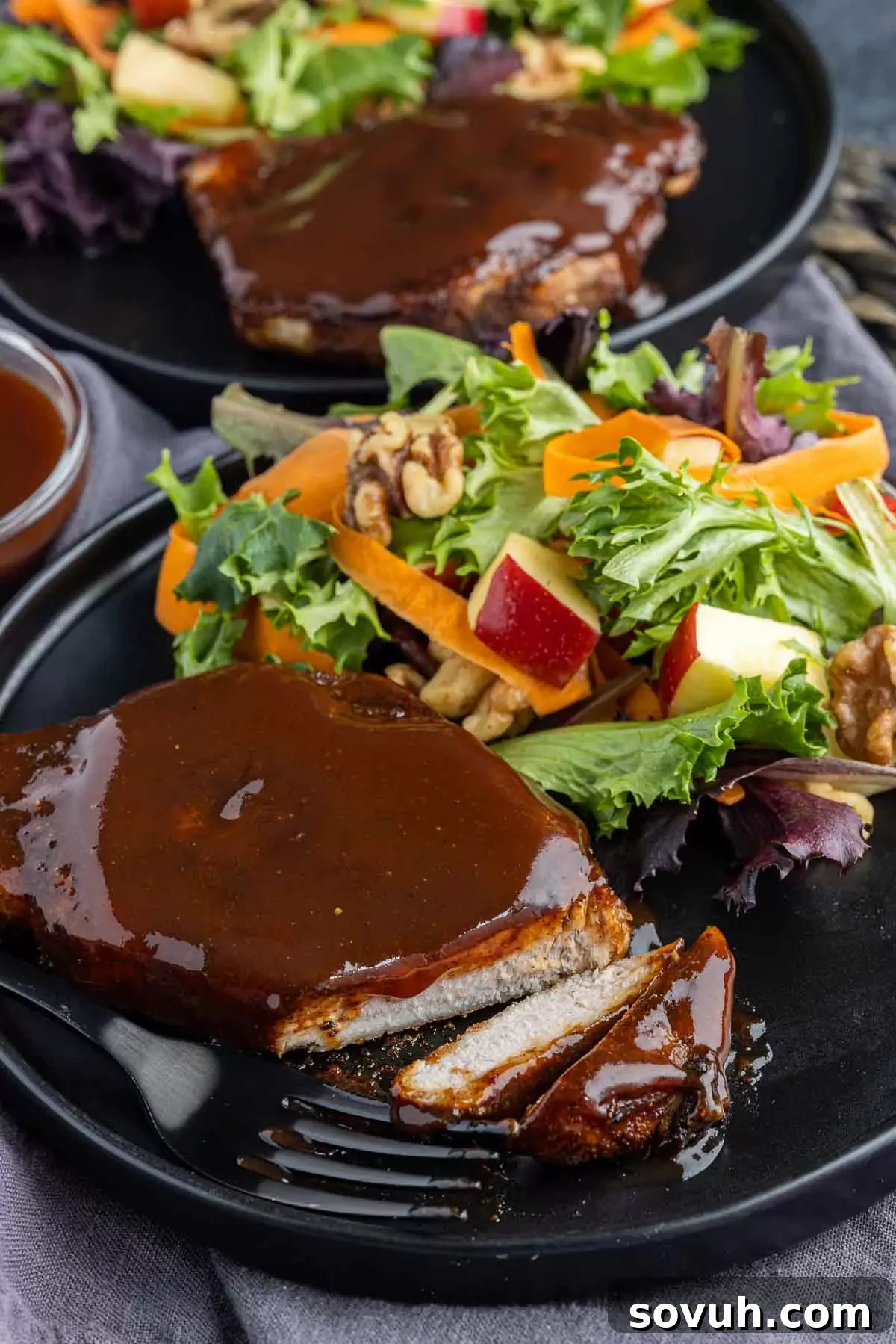 Slices of Air Fryer BBQ Pork Chops arranged on a black plate with a fresh green salad, highlighting a balanced and appealing meal.
