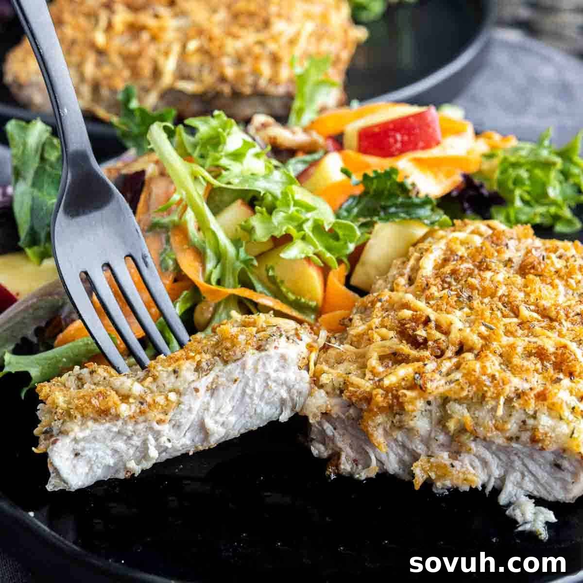 Sliced Air Fryer Parmesan Crusted Pork Chops served with a black fork, showing the tender interior and crispy crust