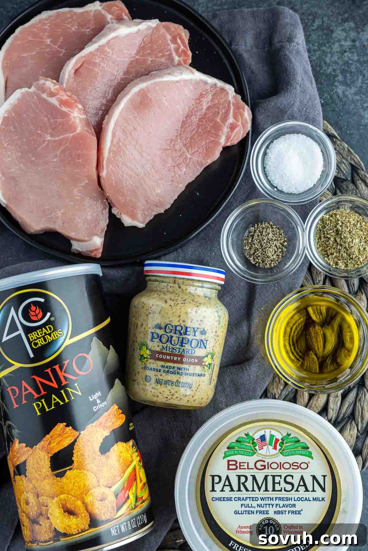 Ingredients for Air Fryer Parmesan Crusted Pork Chops laid out on a table including boneless pork chops, olive oil, spices, Parmesan, Panko, and Dijon mustard