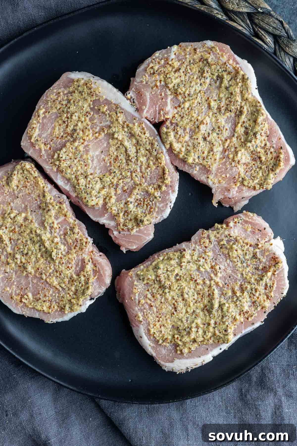 Raw seasoned Air Fryer Parmesan Crusted Pork Chops on a black plate, ready for the next step of coating