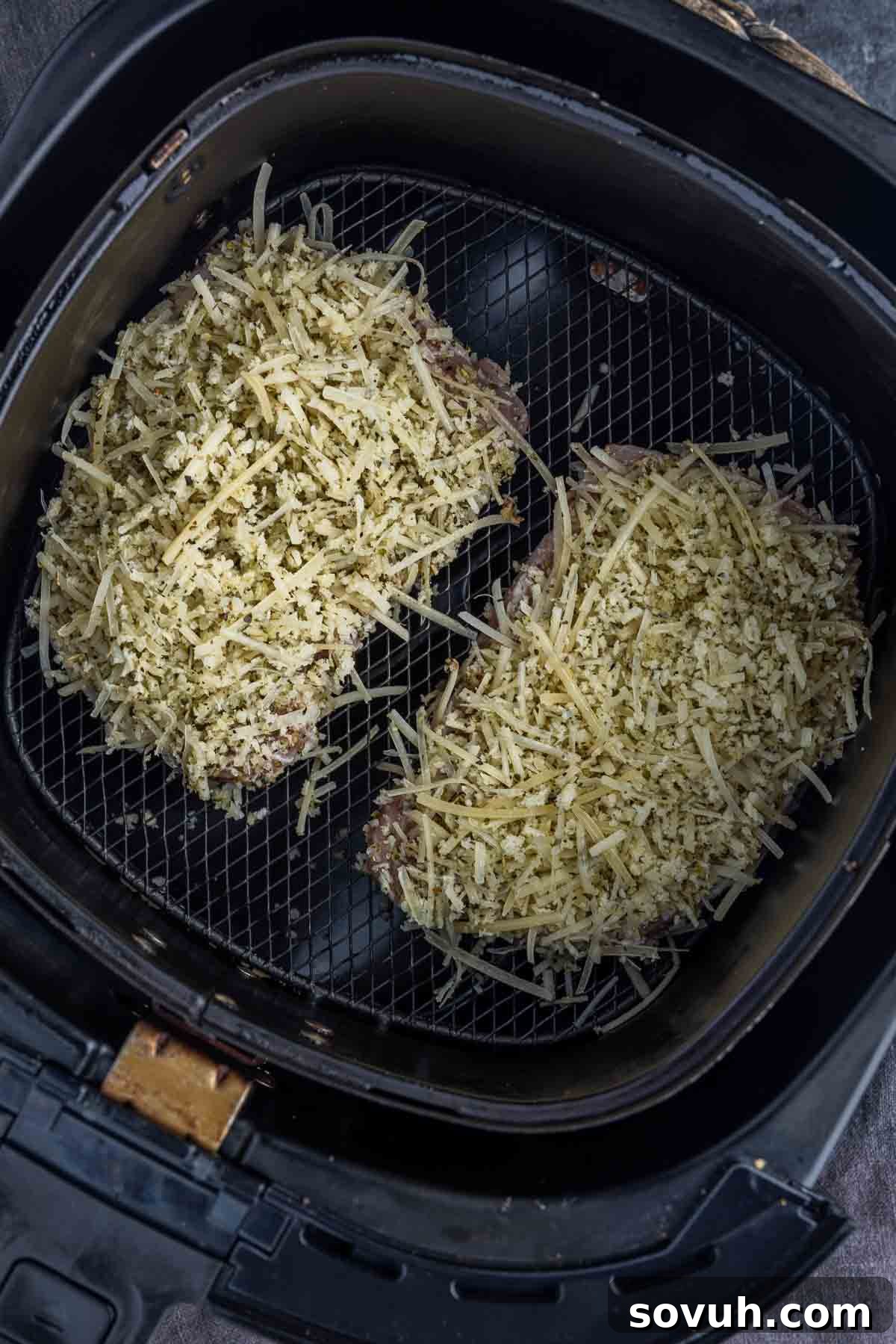 Two raw Air Fryer Parmesan Crusted Pork Chops placed side-by-side in an air fryer basket, ready to cook