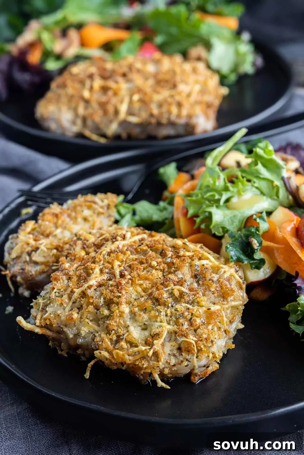 Plated Air Fryer Parmesan Crusted Pork Chops with a side salad on a black plate