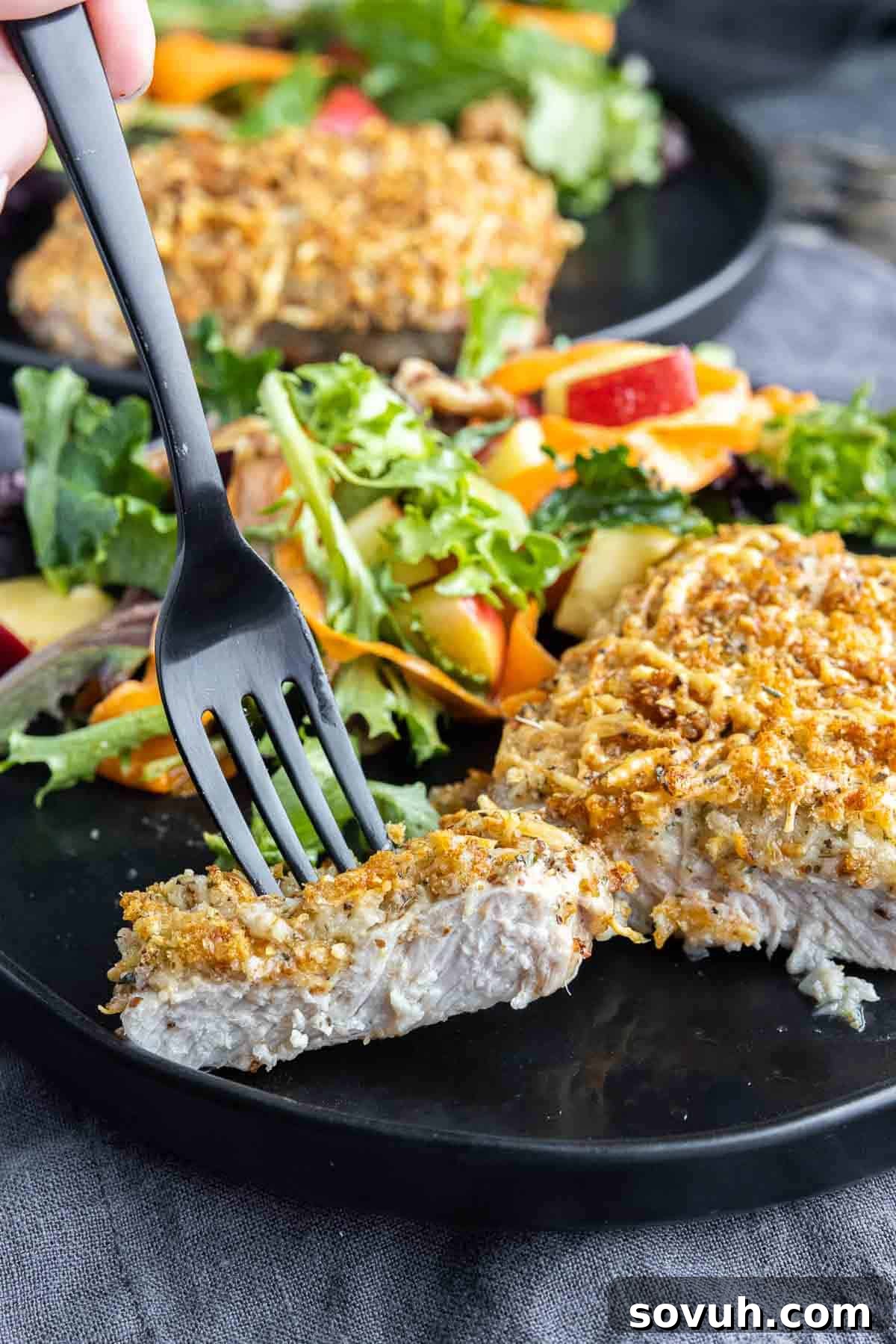 Air Fryer Parmesan Crusted Pork Chop on a black plate with a slice on a black fork, showing its juicy interior